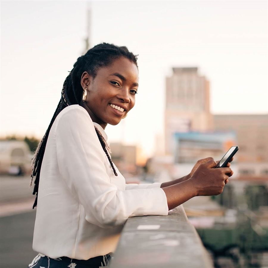 Woman standing on a bridge smiling while holding a phone